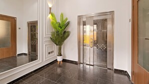 A modern lobby with a large potted plant, a polished marble floor, and a glass elevator door.
