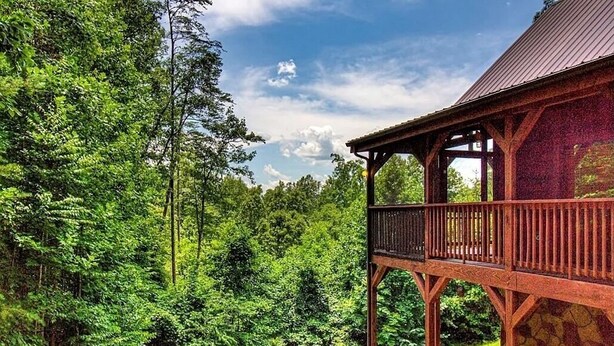 A wooden structure with a balcony overlooking a forested area.