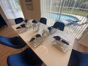 Mesa de jantar posta para seis, com pratos brancos, copos transparentes e guardanapos azuis.