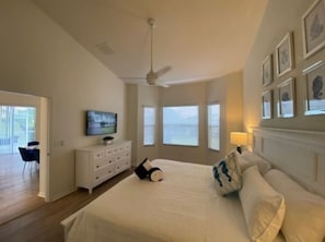 Quarto com cama grande, ventilador de teto, cômoda, televisão e quadros nas paredes.
