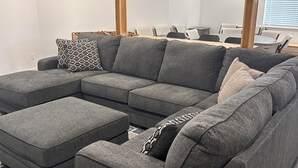 Un salon moderne avec un canapé d’angle, des poufs et un tapis à motifs.