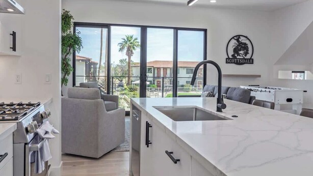 Una cocina moderna con una isla grande, un área de comedor con sofá y vistas al exterior.
