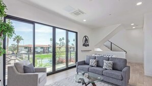 Un salón moderno con un sofá gris, una mesa de centro de vidrio y un gran ventanal corredero que da a un balcón.