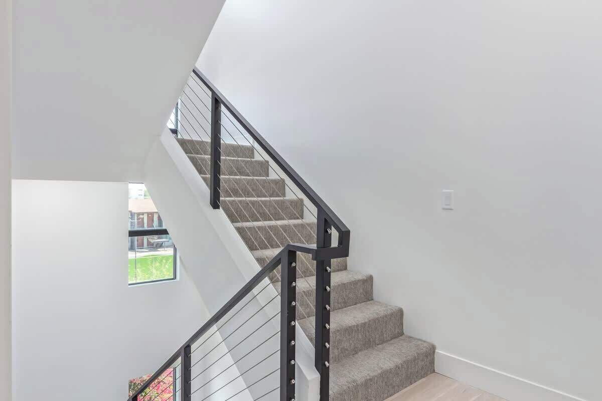 A modern staircase with a geometric design, a small window, and a plain wall.