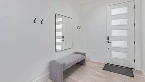 Un pasillo moderno con un banco, una puerta con paneles de vidrio esmerilado y un espejo en la pared.