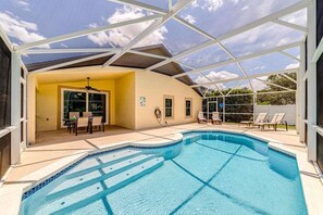 Uma piscina com um terraço coberto, uma mesa de jantar e cadeiras de descanso.