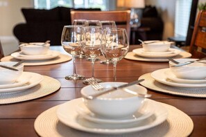 Mesa de jantar posta com pratos, tigelas e copos de vinho brancos, com uma cadeira ao fundo.