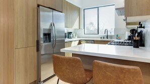 Eine moderne Küche mit Holzausstattung, einem Edelstahlkühlschrank, einer weißen Arbeitsplatte und zwei braunen Stühlen.