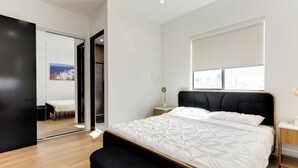 Ein modernes Schlafzimmer mit einem großen Bett, einem Nachttisch, einem Spiegel und einer Schiebetür zu einem weiteren Raum.