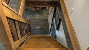 A wooden staircase with a handrail, leading to a landing with a light-colored wall and a dark wooden floor.