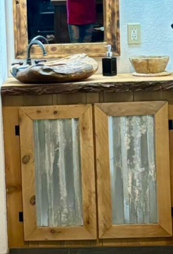 A rustic kitchen with a wooden countertop, a large bowl, and a mirror above the sink.