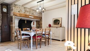 Un comedor con pared de piedra, sillas de madera, una mesa blanca y un reloj.
