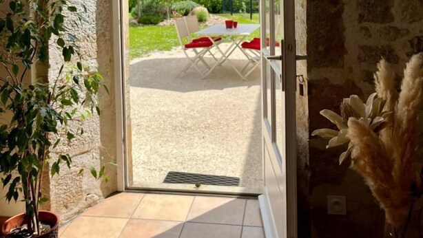 Una habitación con pared de piedra, una planta en maceta y vistas a un patio exterior con mesa y sillas.