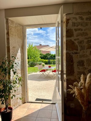 Une pièce avec un mur en pierre, une plante en pot et une vue sur une terrasse extérieure avec une table et des chaises.