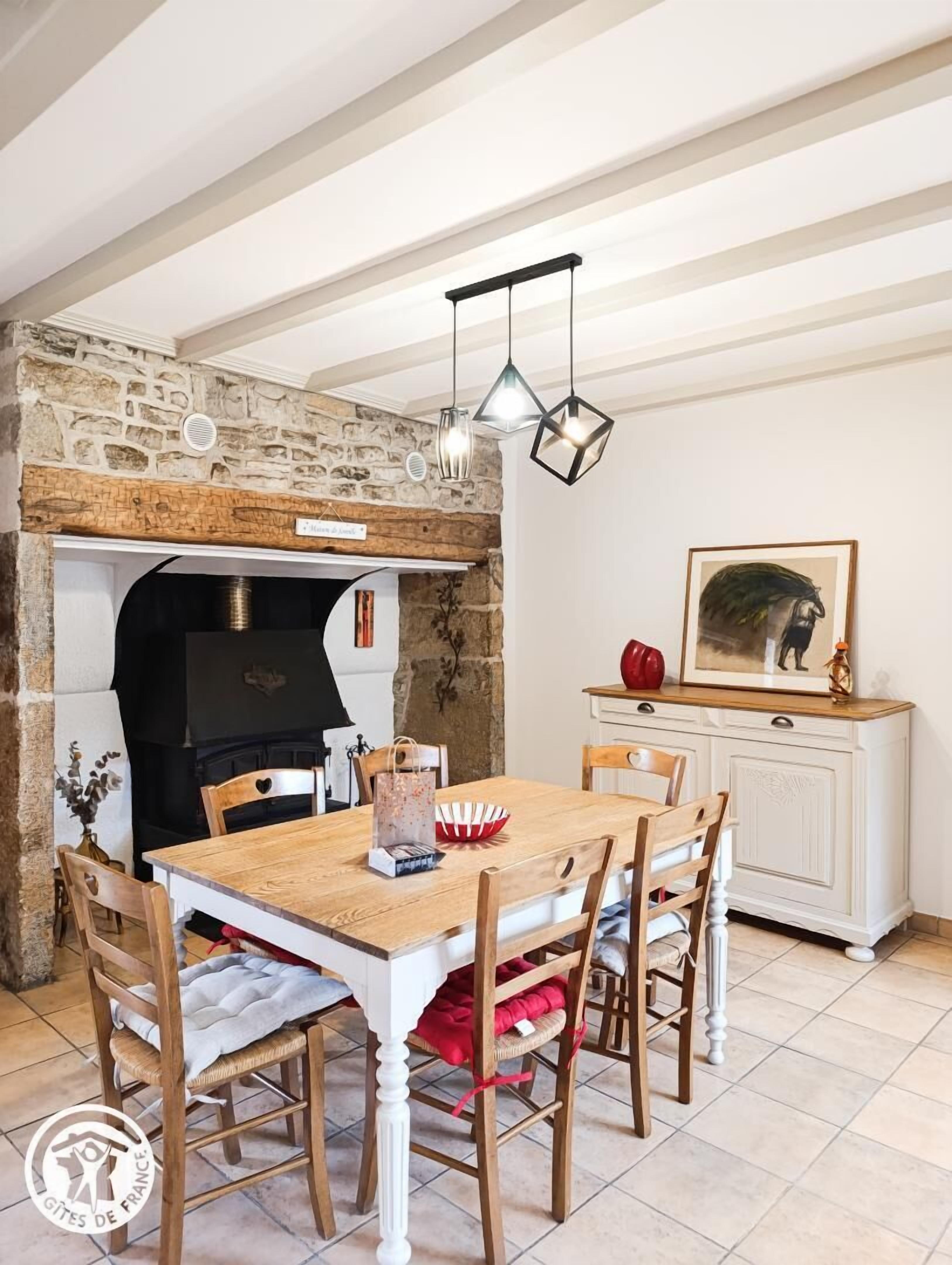 A rustic dining area with a stone fireplace, wooden table, and chairs.