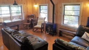 A cozy cabin interior with wooden walls, a fireplace, leather sofas, and large windows. - Blue Loon Camp on Pleasant Pond in Litchfield (Litchfield)