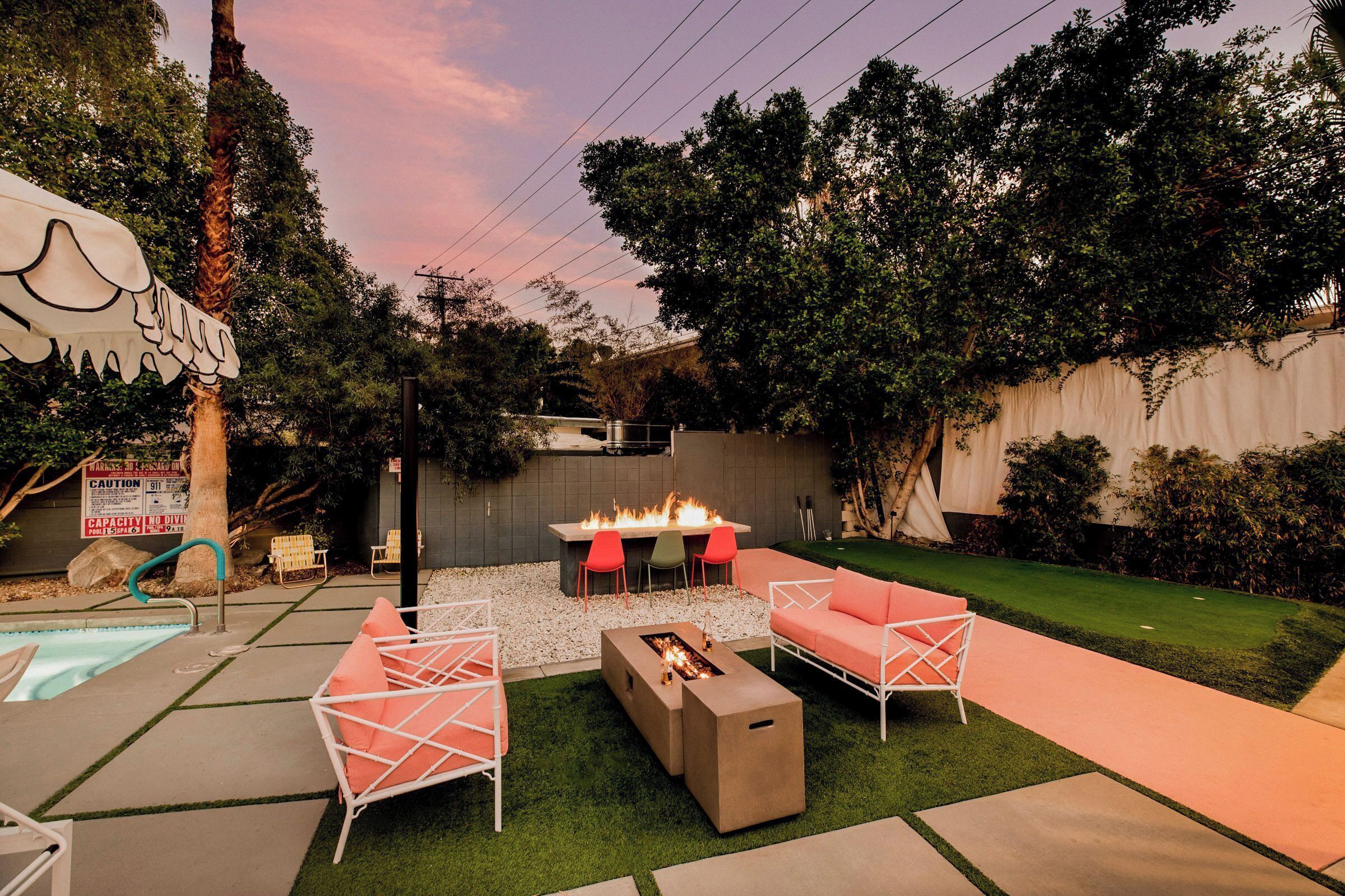 Un jardin avec un foyer extérieur, un espace salon de jardin, une piscine et une pelouse bien entretenue.