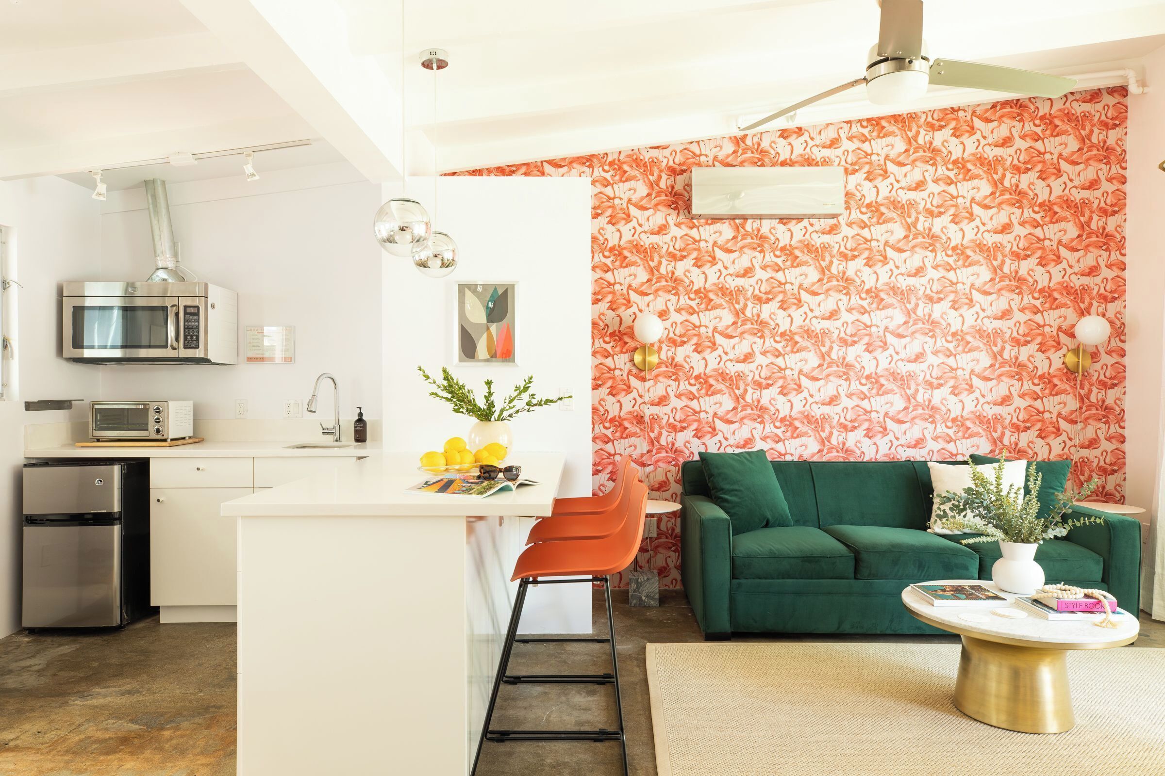 A compact living space with a kitchenette, a green sofa, a coffee table, and a vibrant floral wallpaper.