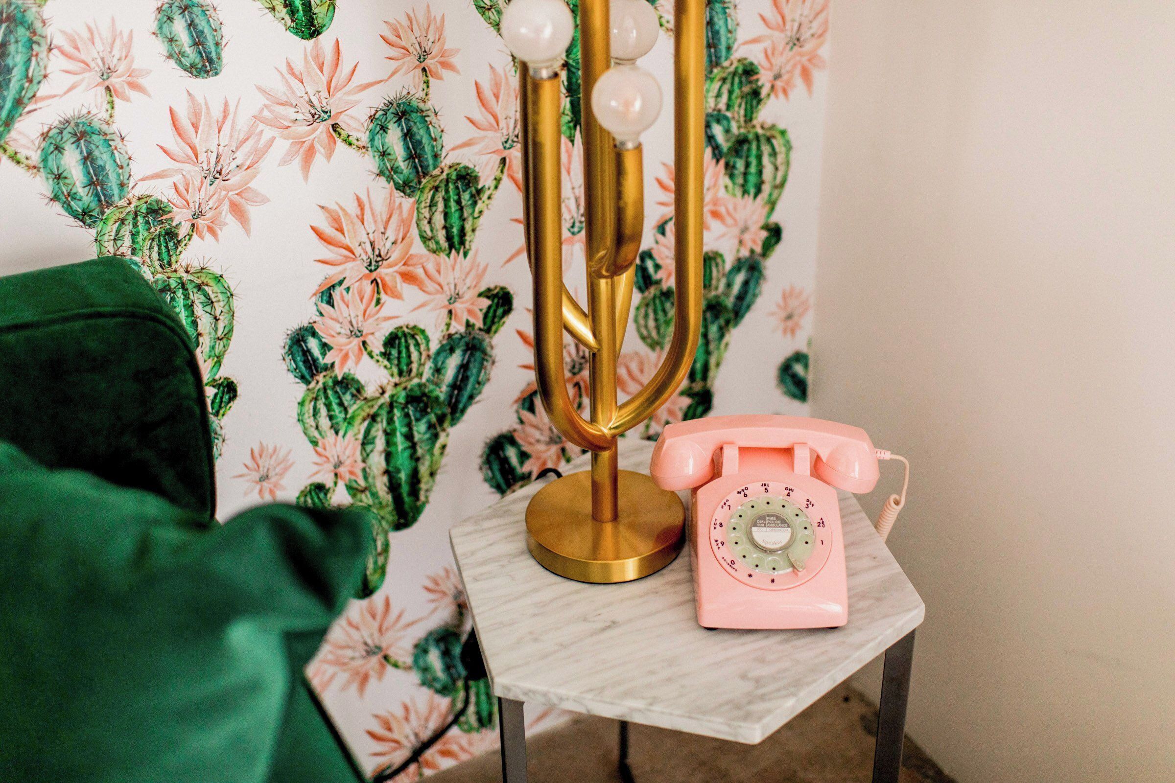 A vintage-style telephone on a marble table, a golden lamp with three white spherical lights, and a green chair.