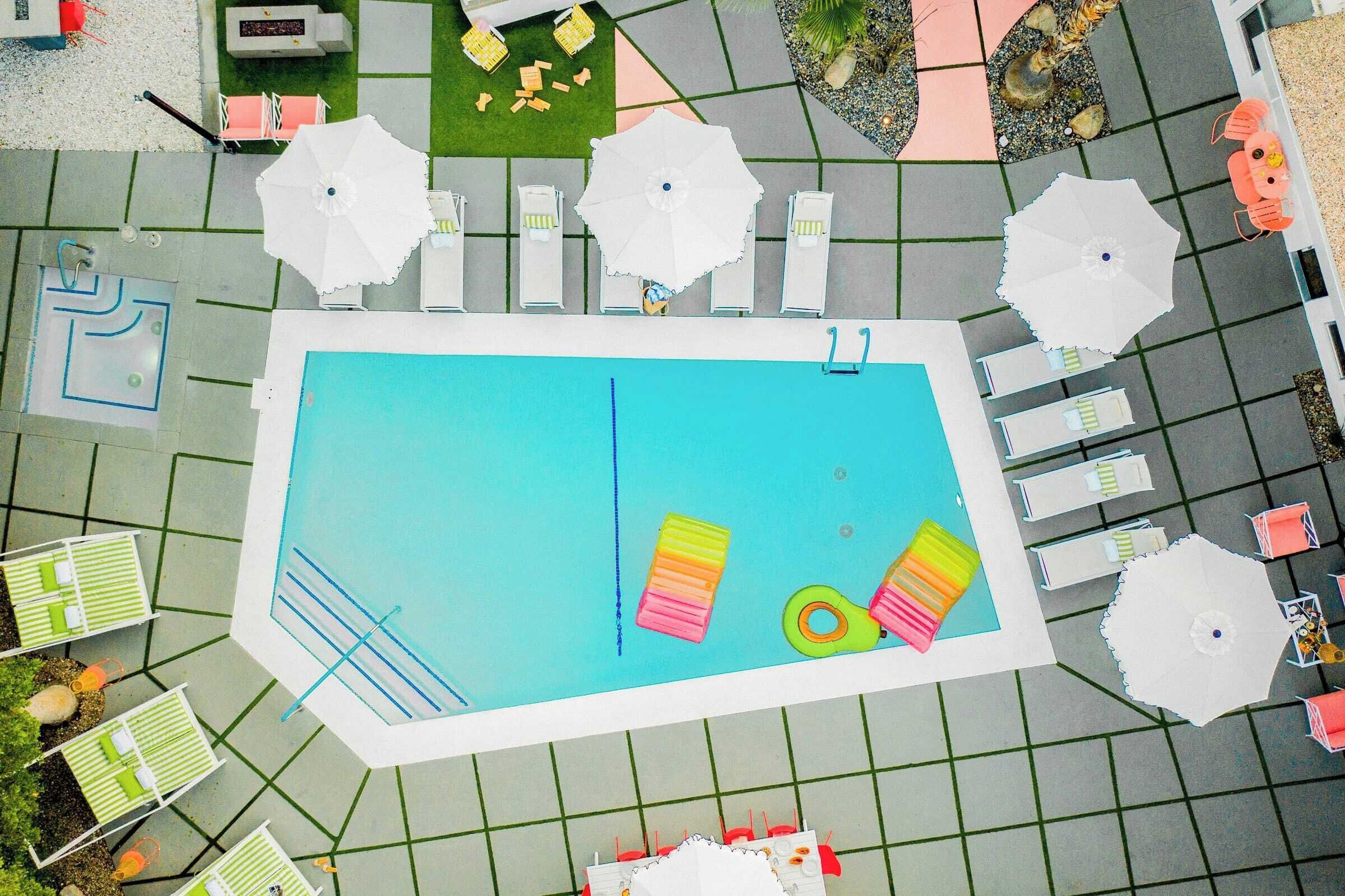Vista aérea de una zona de piscina con múltiples sillones de descanso y sombrillas.
