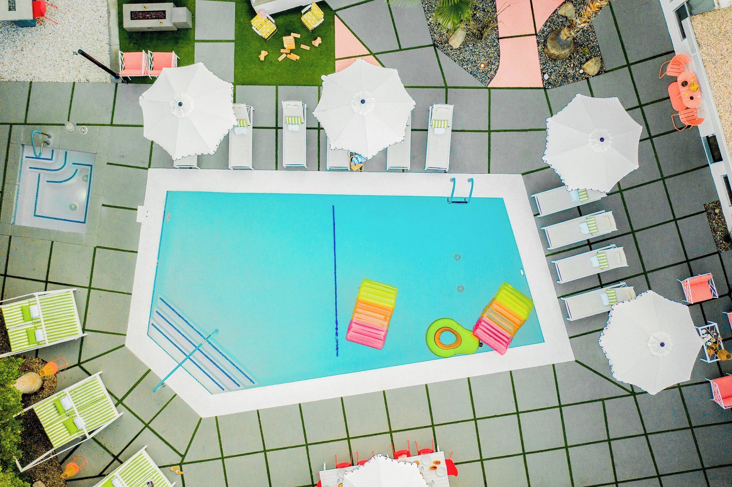 Eine Vogelperspektive auf einen Swimmingpool mit angrenzenden Liegestühlen und Sonnenschirmen, umgeben von einer gefliesten Terrasse.