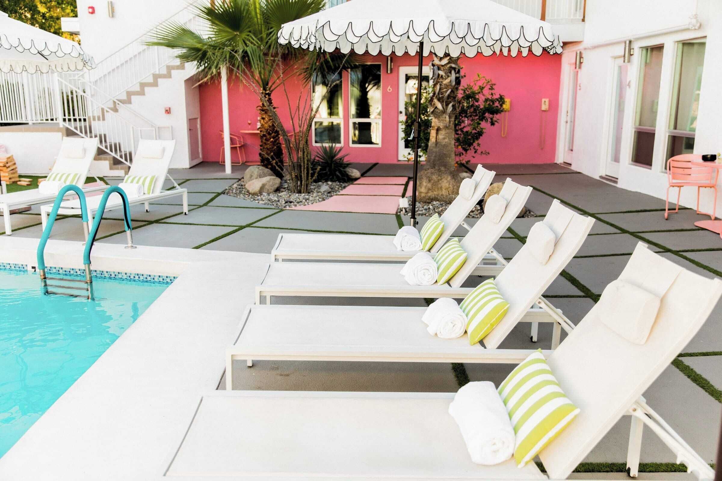 A pool area with white lounge chairs and a pink building in the background.