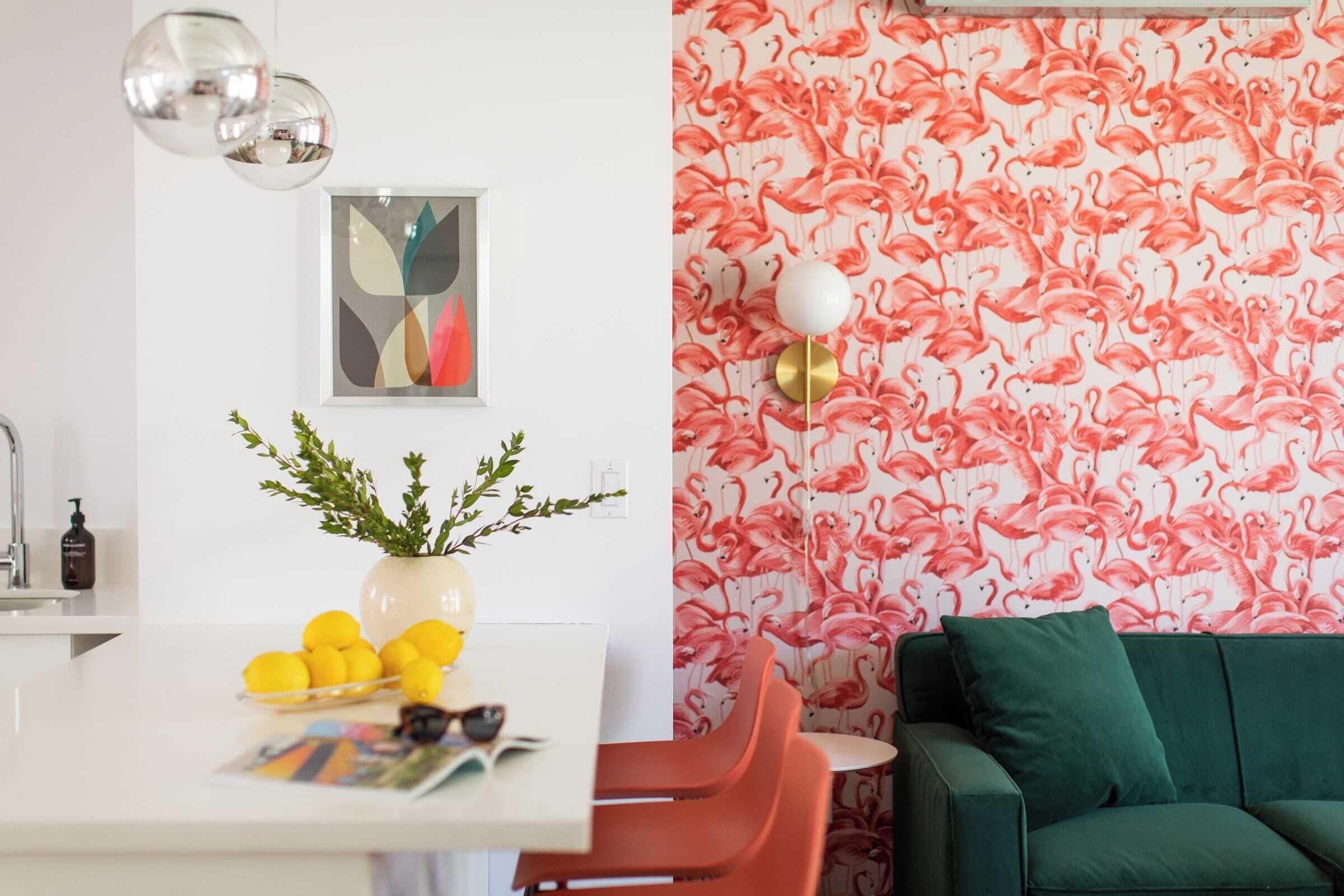 A dining area with a white table, red chairs, a vase with greenery, and a framed abstract painting.
