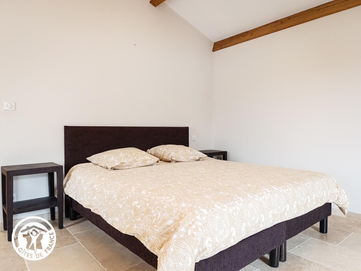 A bedroom with a bed, two bedside tables, and a wooden ceiling beam.