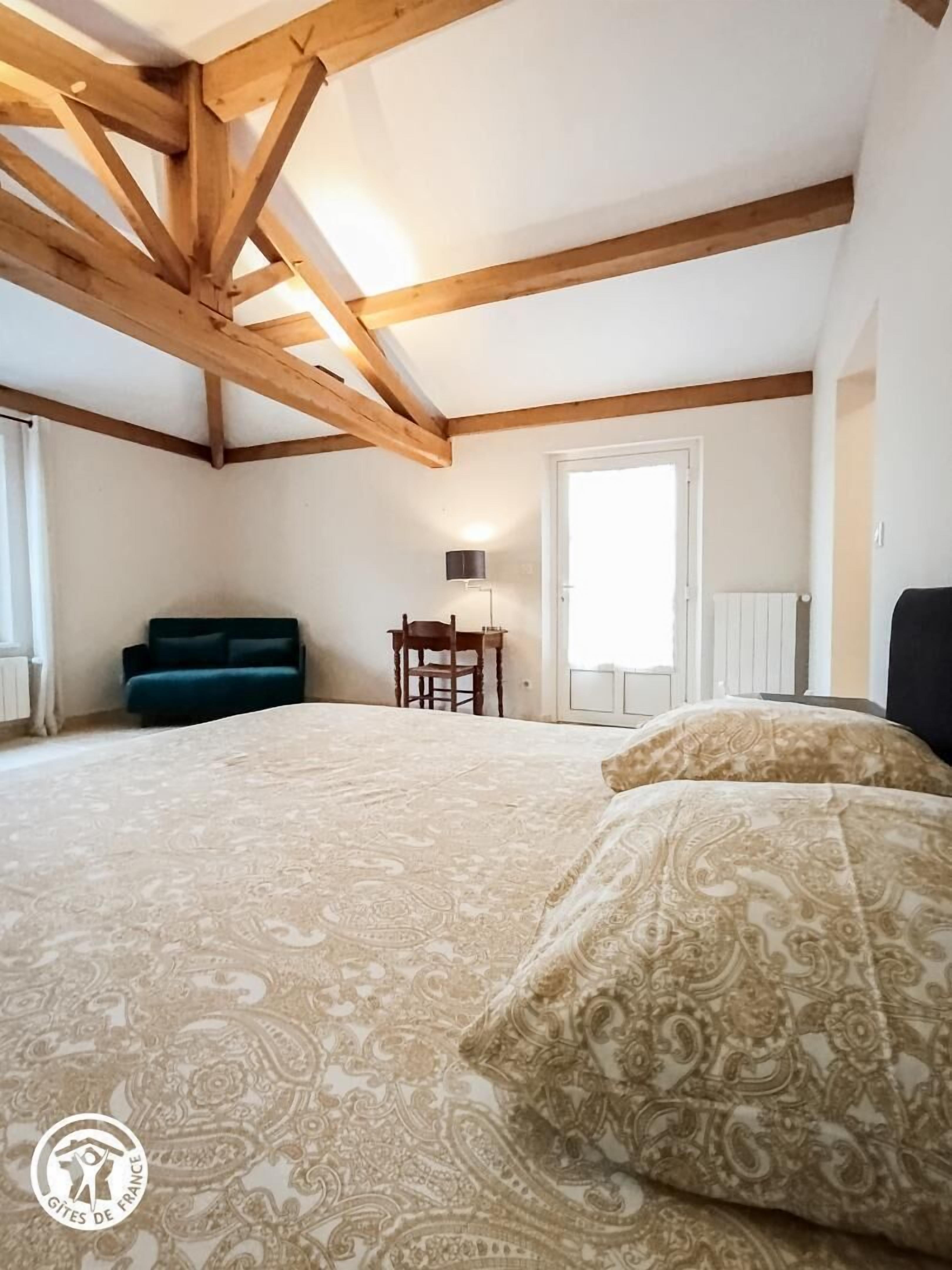 Ein Schlafzimmer mit einem großen Bett, Holzboden, einem Stuhl, einer Lampe und einem Fenster.