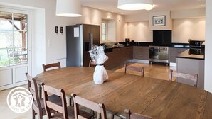 A modern kitchen with a dining area, featuring a wooden table, chairs, a refrigerator, and a stove.