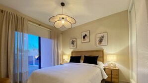 A bedroom with a large bed, two bedside tables with lamps, a ceiling light fixture, and a view of the outdoors through a window with curtains. - Charming 1-bedroom apartment with AC, WiFi and amazing views in Mojácar (Mojácar)