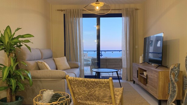A living room with a sofa, a wicker chair, a television, and a large window with a view of the sea. - Charming 1-bedroom apartment with AC, WiFi and amazing views in Mojácar (Mojácar)