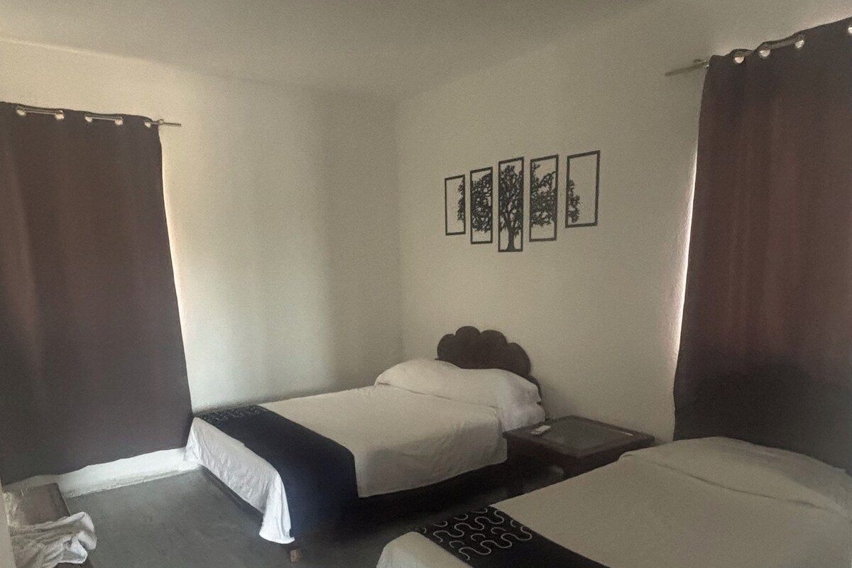 A room with two beds, a small table, and a wall-mounted picture frame.