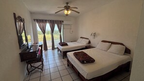 A hotel room with two beds, a desk, a chair, a ceiling fan, and a window with curtains. - Hotel Costa Bugambilias (Manzanillo)