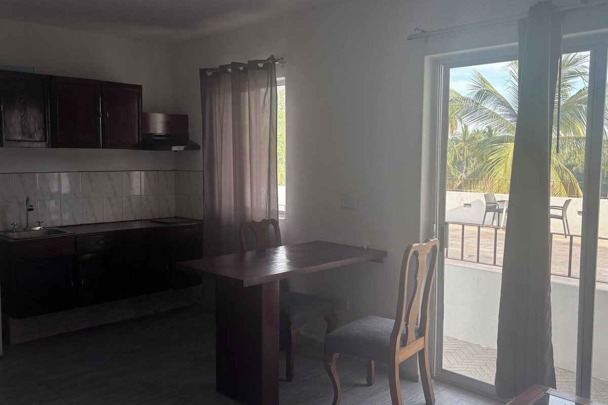 Una cocina con armarios oscuros, un salpicadero azulejado y una zona de comedor con mesa y sillas.