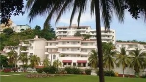 Un hotel a più piani con tetto piatto, circondato da palme e un prato curato.