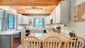 A compact kitchen with wooden cabinets, a microwave, a sink, and a dining area with two wooden chairs. - A 3 Story, 3 Bedroom Traditional Rustic Ski and Hiking Chalet (Deming)