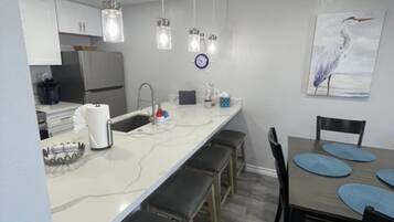 Une cuisine moderne avec des plans de travail blancs, des appareils en acier inoxydable et des luminaires suspendus.