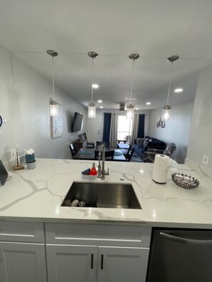A modern kitchen with a large island, stainless steel sink, and overhead pendant lighting. - Ocean Front Condo @ Hello Summer - Galveston (Galveston)