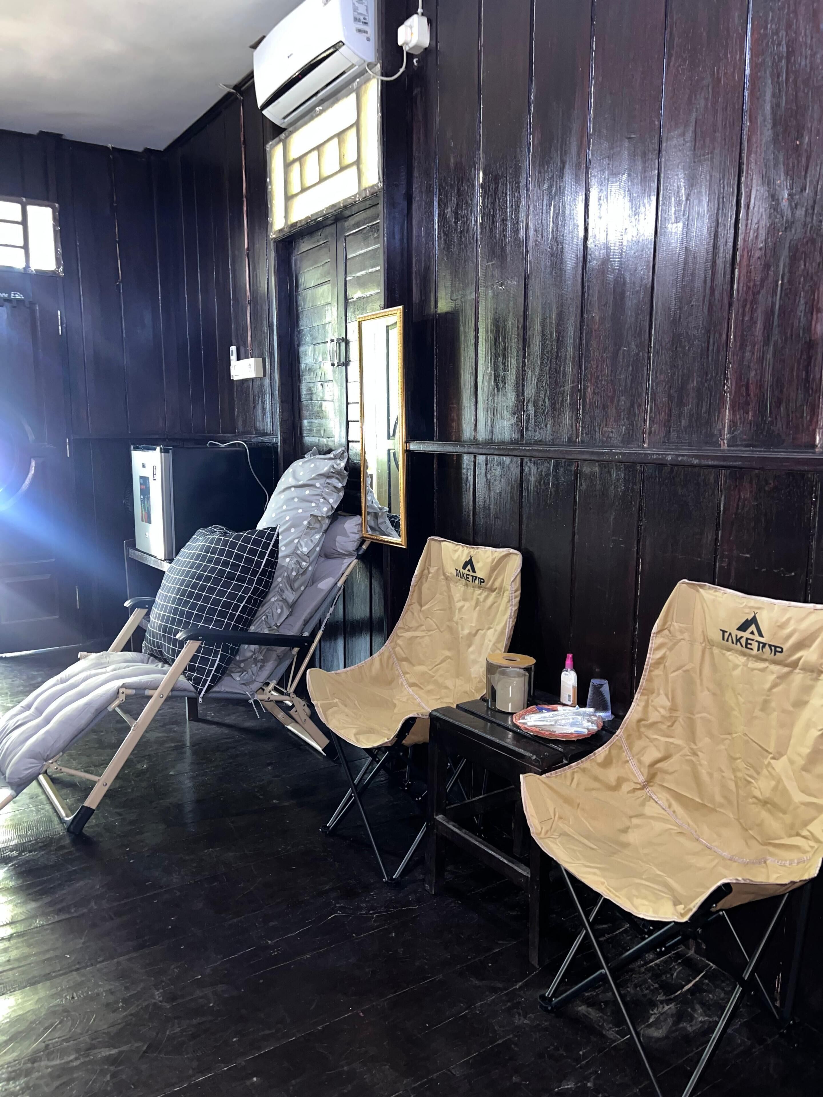 Une pièce avec un mur en bois foncé, une fenêtre, un ventilateur de plafond et une table avec une chaise.