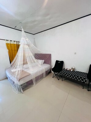 A room with a bed under a mosquito net, a small table with a black tablecloth, and a chair. - Charming villa with 1 bedroom and AC, WiFi, in phenomenal Raja Ampat (RAJA AMPAT)