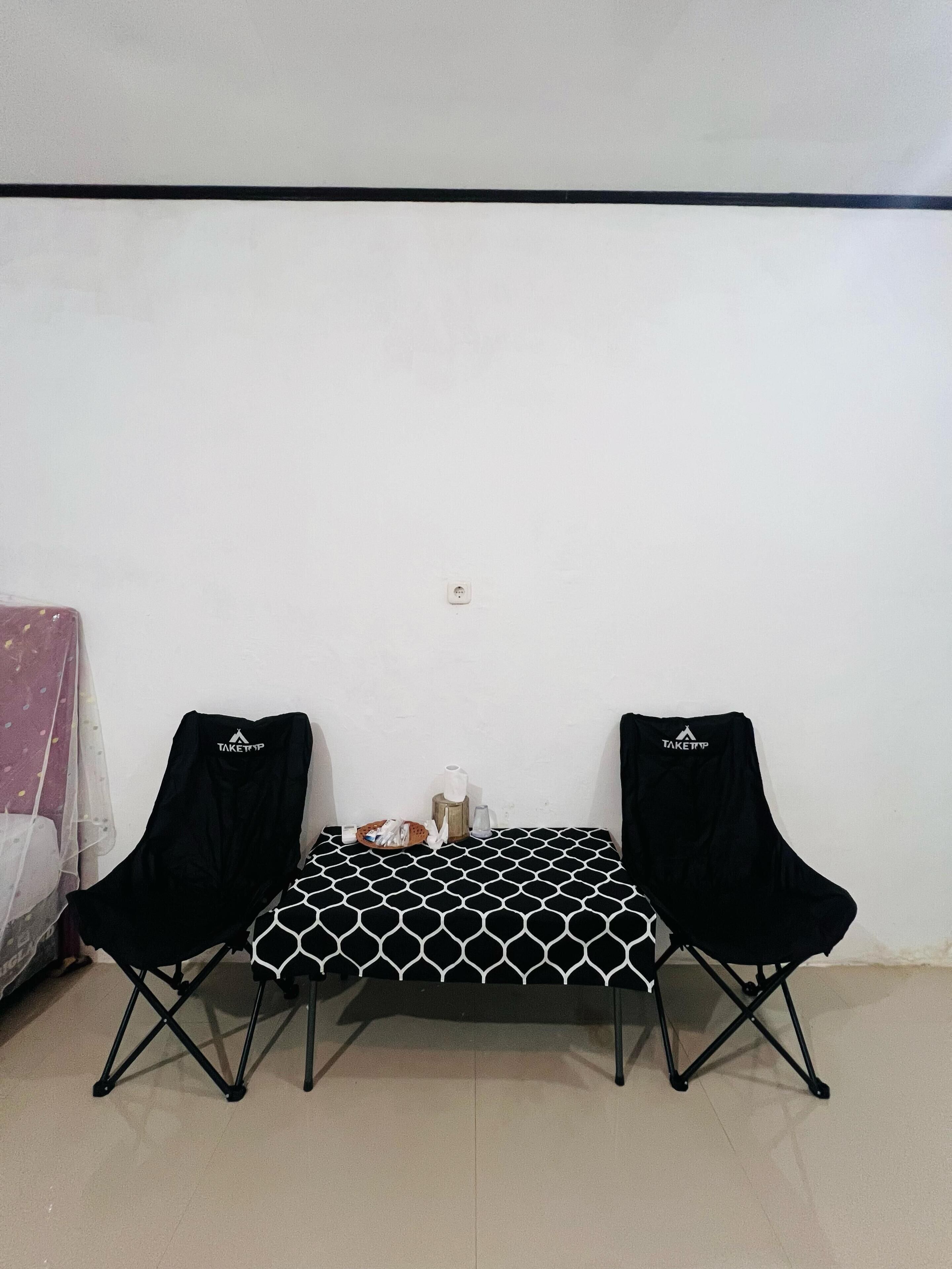A small room with a white wall, a black and white patterned table, and two black chairs.
