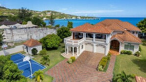 Una casa grande con cancha de tenis, piscina y vista al océano.
