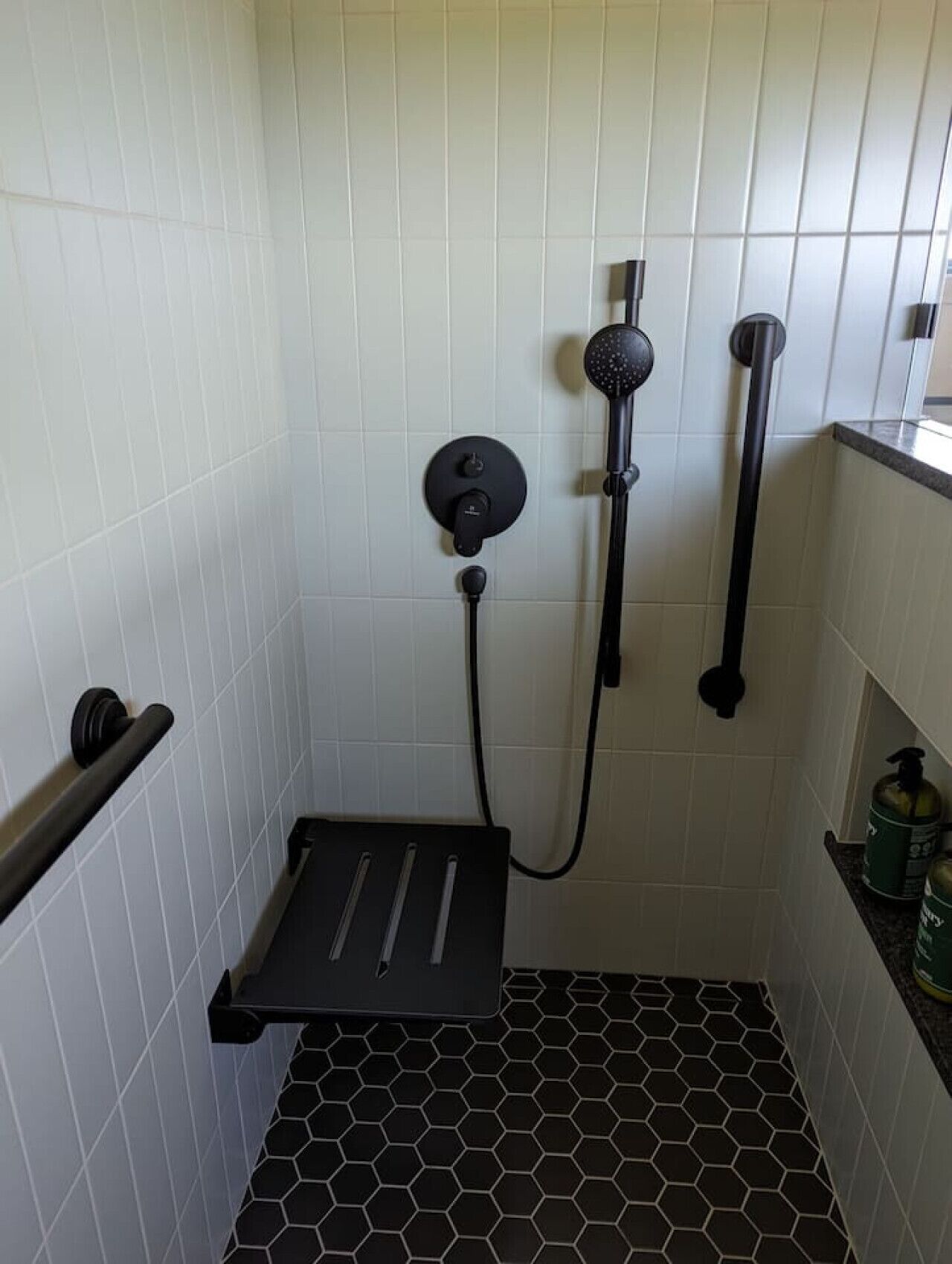 Zona de ducha con cabezal de ducha negro, ducha de mano y panel de control.