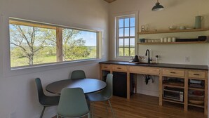 Une cuisine avec une table et des chaises, des meubles en bois, une fenêtre donnant sur des arbres et un luminaire suspendu.