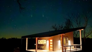 Une maison moderne à deux étages, dotée d’un patio couvert, de grandes fenêtres et offrant une vue sur un ciel étoilé.