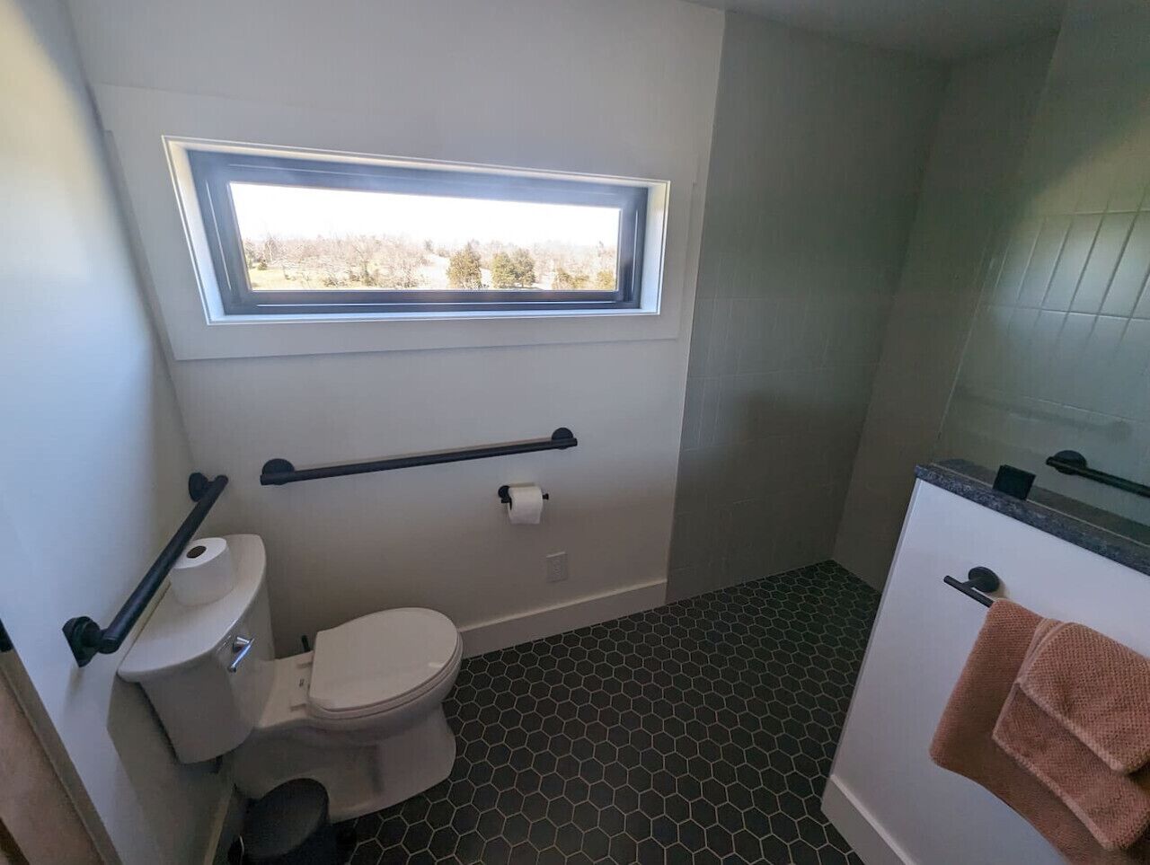 Een badkamer met toilet, een raam, een handdoekhouder en een douchehoek.