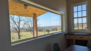 A room with a large window overlooking a landscape, a wooden ceiling, and a simple desk with drawers. - Your Own Two Cabin Retreat (Frankfort)