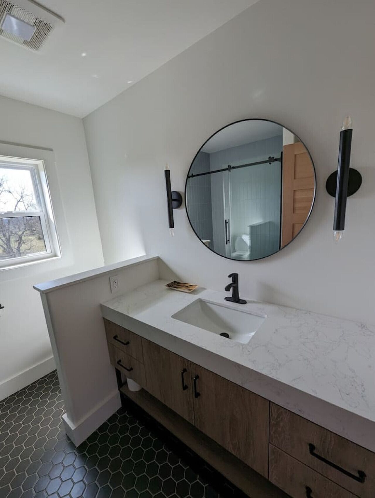 A modern bathroom with a white vanity, a round mirror, and a black faucet.
