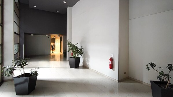 A spacious hallway with modern architecture, featuring large potted plants and a fire extinguisher on the wall. - Merced Plaza Apart (Santiago)